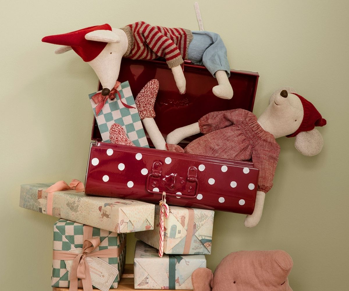 Stuffed toys in a suitcase with wrapped presents on a light green background