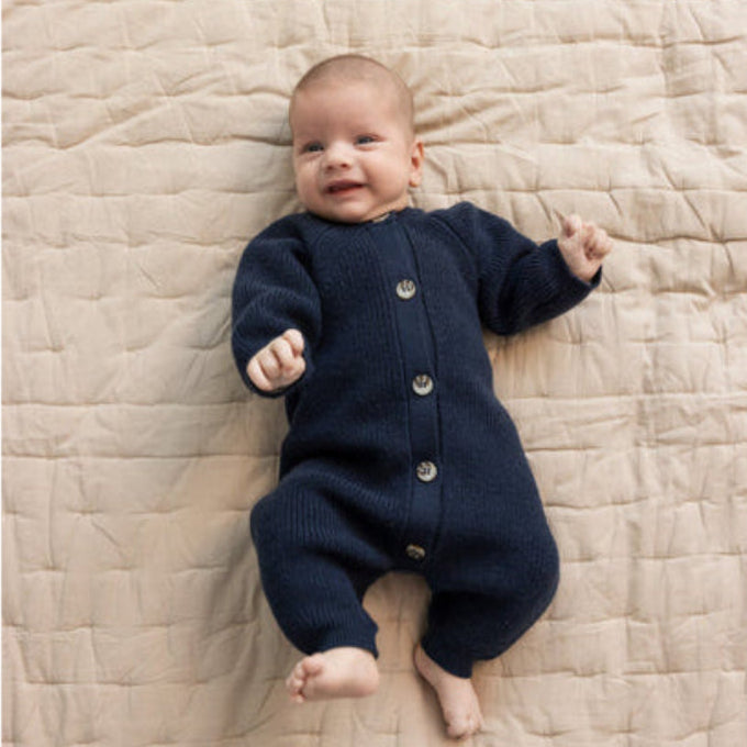 Baby wearing a navy blue outfit lying on a beige quilted blanket