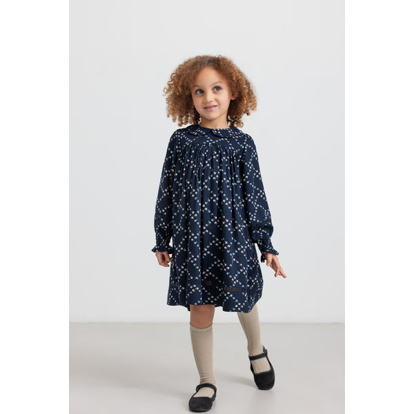 Child wearing a navy dress with white patterns on a white background
