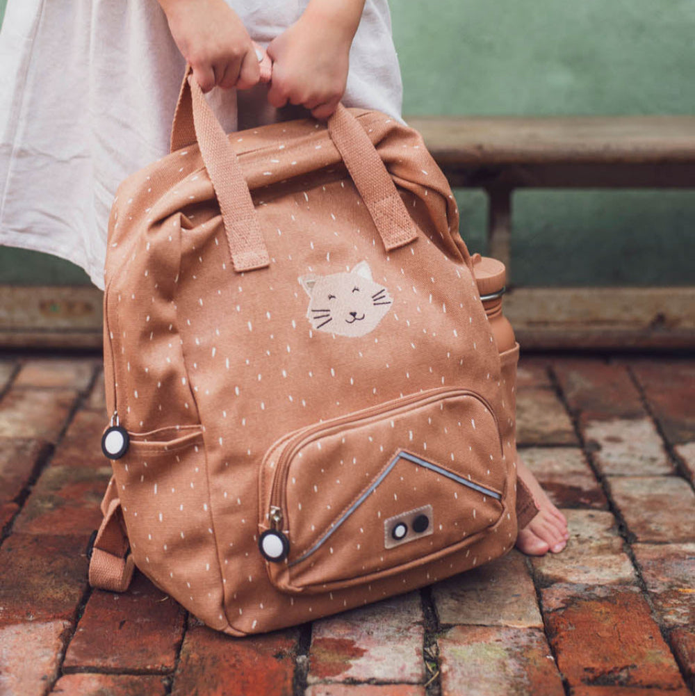 Person holding a brown backpack with a cat design on a brick floor.