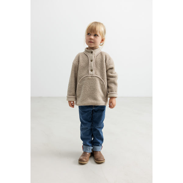 Child wearing a beige fleece jacket and blue jeans on a white background