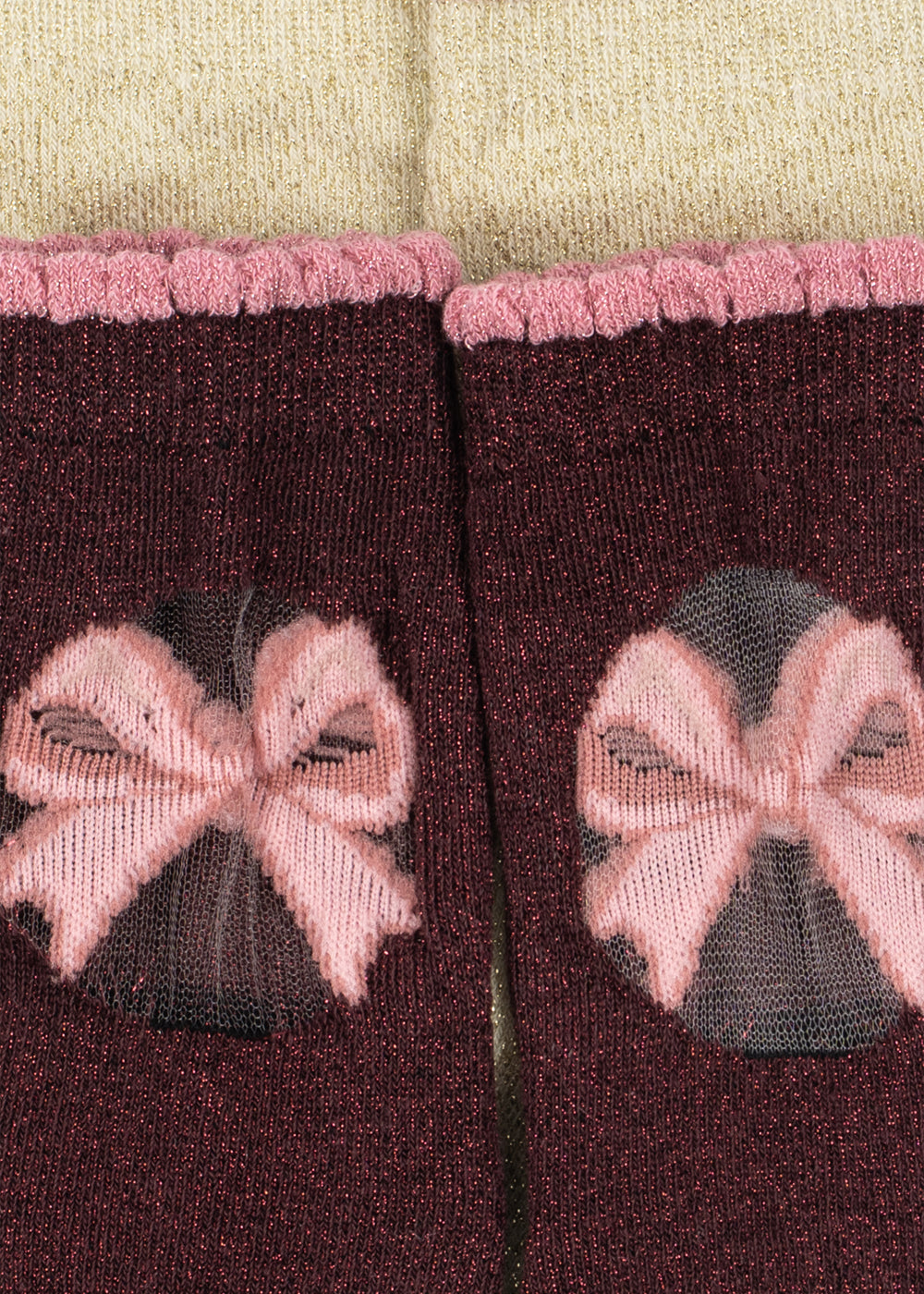 A close-up of a pair of dark burgundy knit socks with pink ribbed cuffs and a pink bow motif on the front, set against a cream-colored knit background.