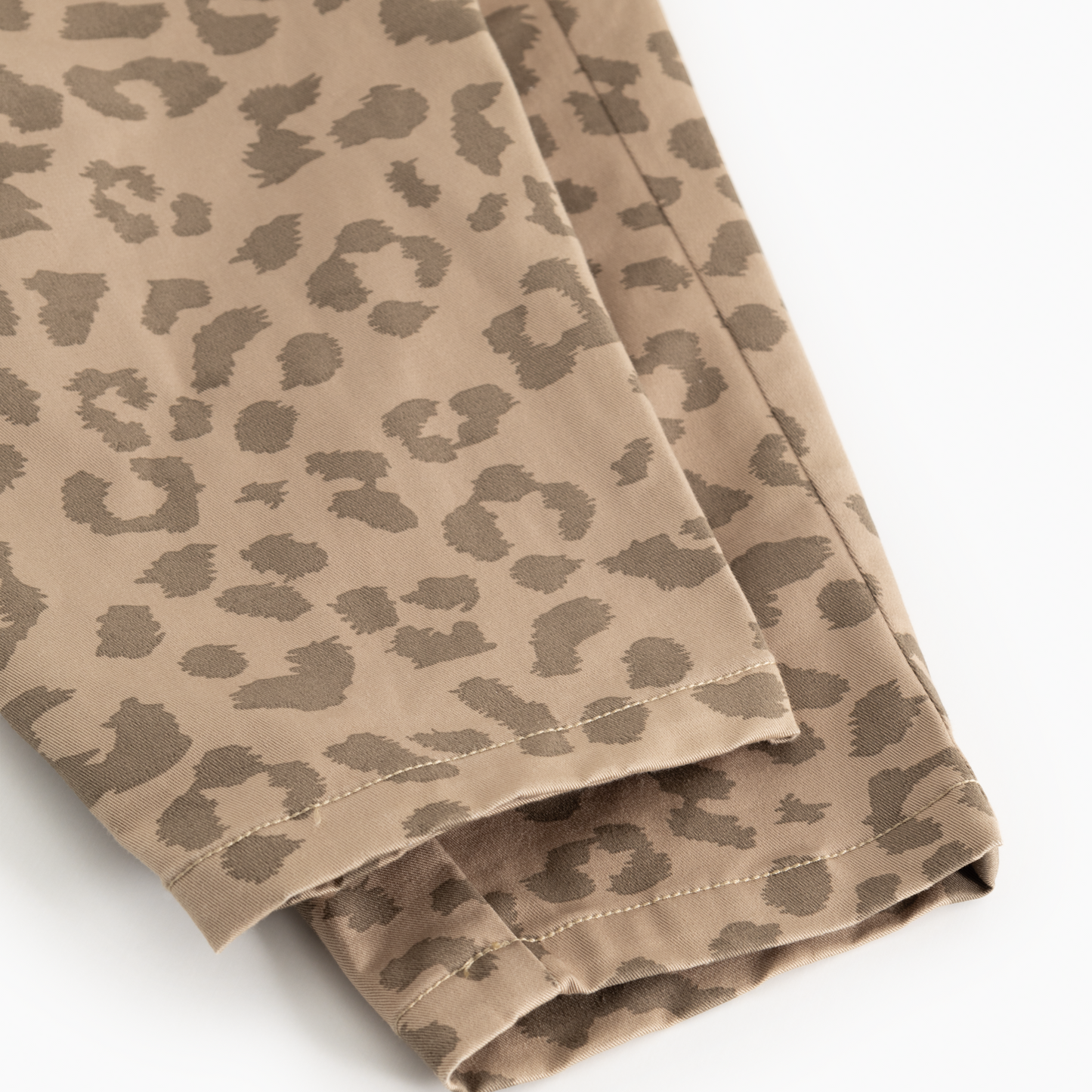 Close-up of a beige and brown leopard print fabric, showing the texture, stitching, and folded edges of a garment on a white background.
