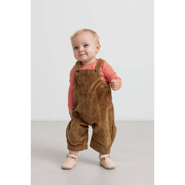 Baby wearing brown corduroy overalls and a red striped shirt on a white background, by Mar mar Copenhagen