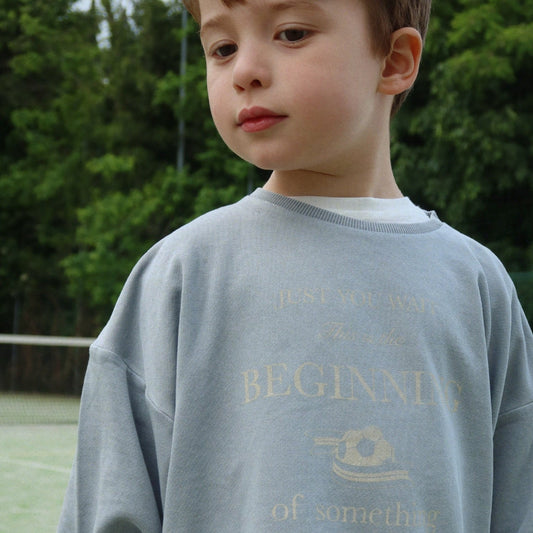 Boy wearing organic cottona gray sweatshirt with text and logo outdoors