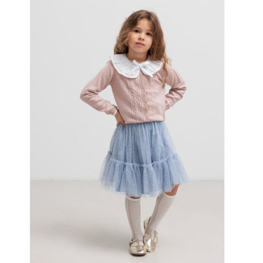 Young girl wearing a pink blouse with a white collar and a blue ruffled skirt on a light gray background