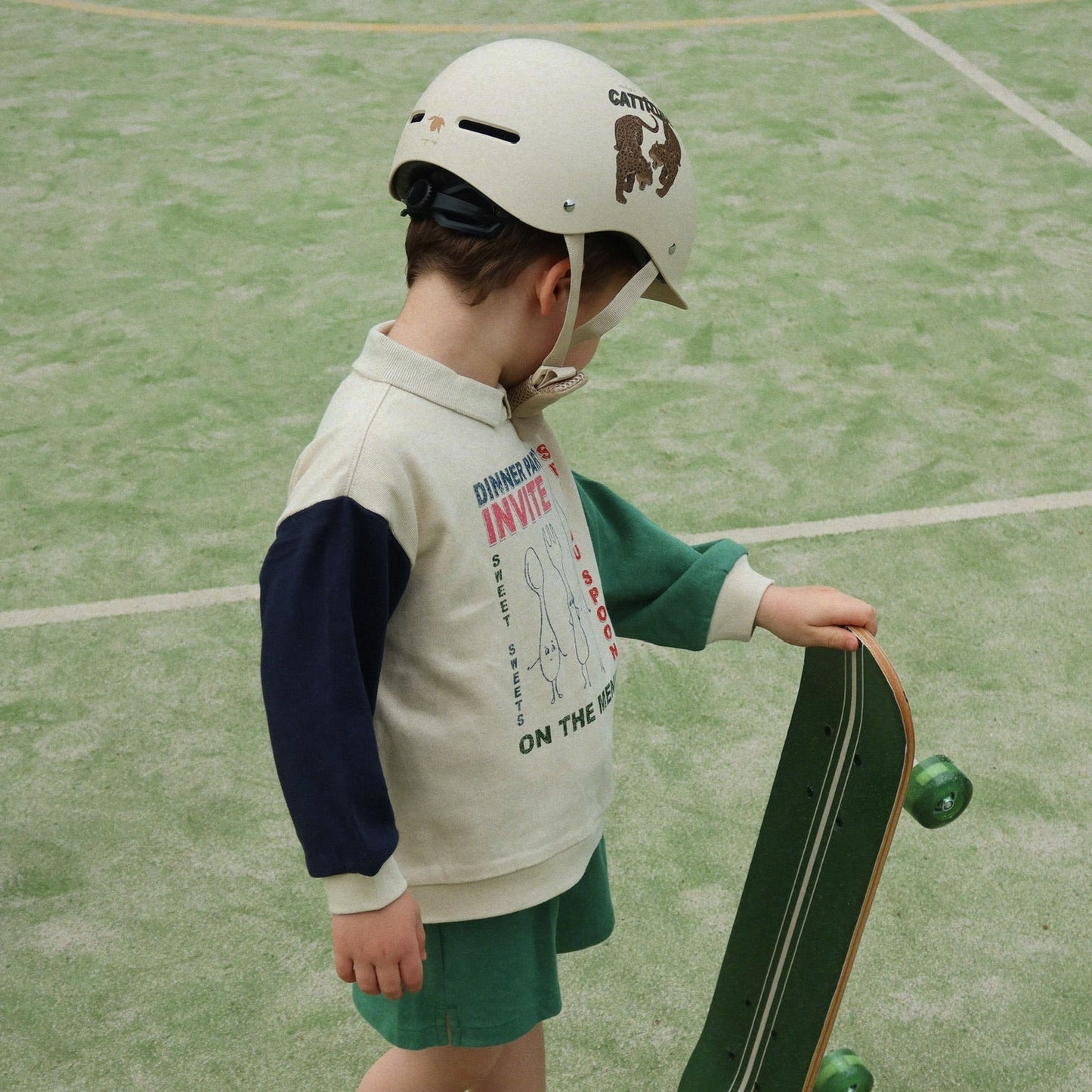 Child wearing a helmet and holding a skateboard on a green court