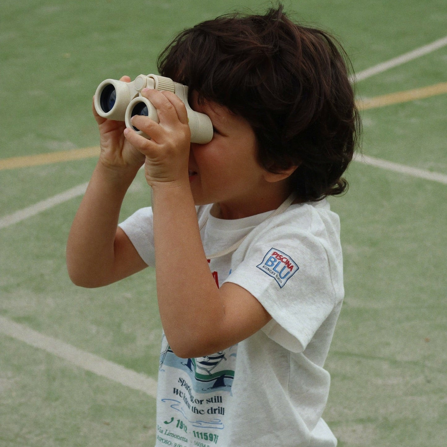 Child holding binoculars on a sports field