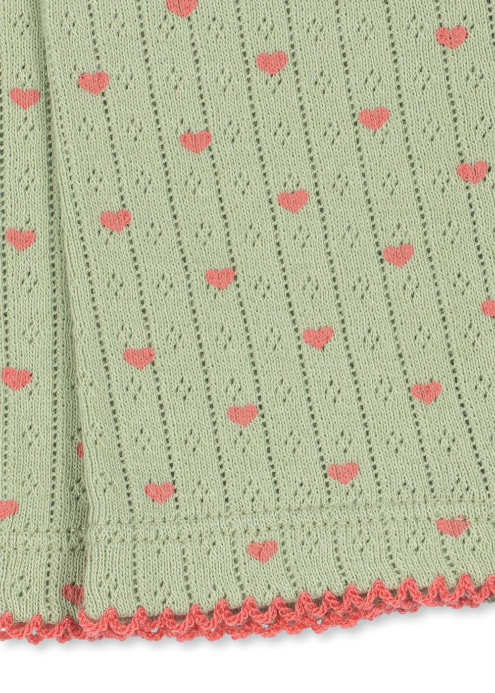 Close-up of a light sage green knit fabric with a repeating pattern of small pink hearts and a pink scalloped edge.