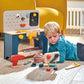 Child playing with a wooden toy workbench in a room with a yellow chair.
