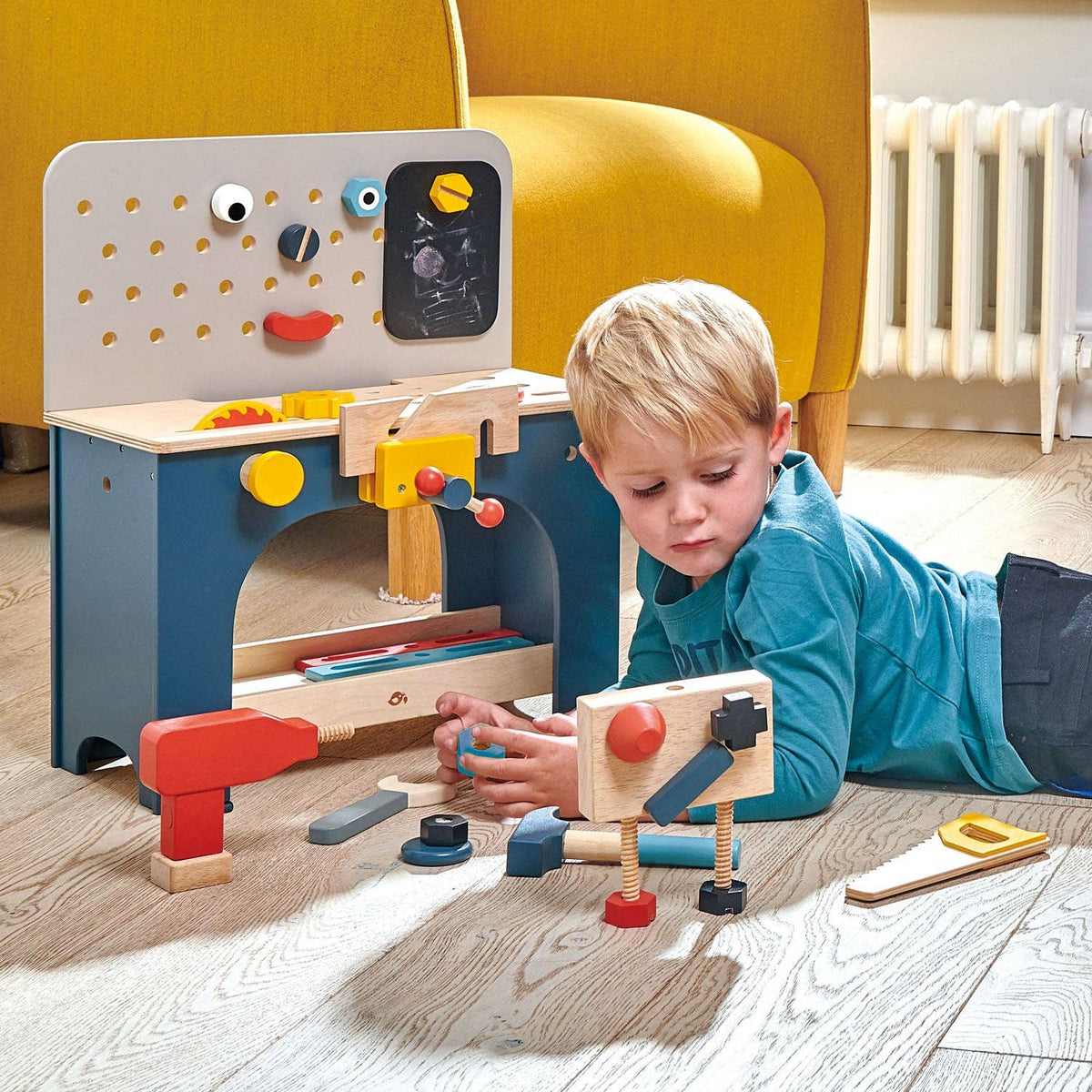 Child playing with a wooden toy workbench in a room with a yellow chair.