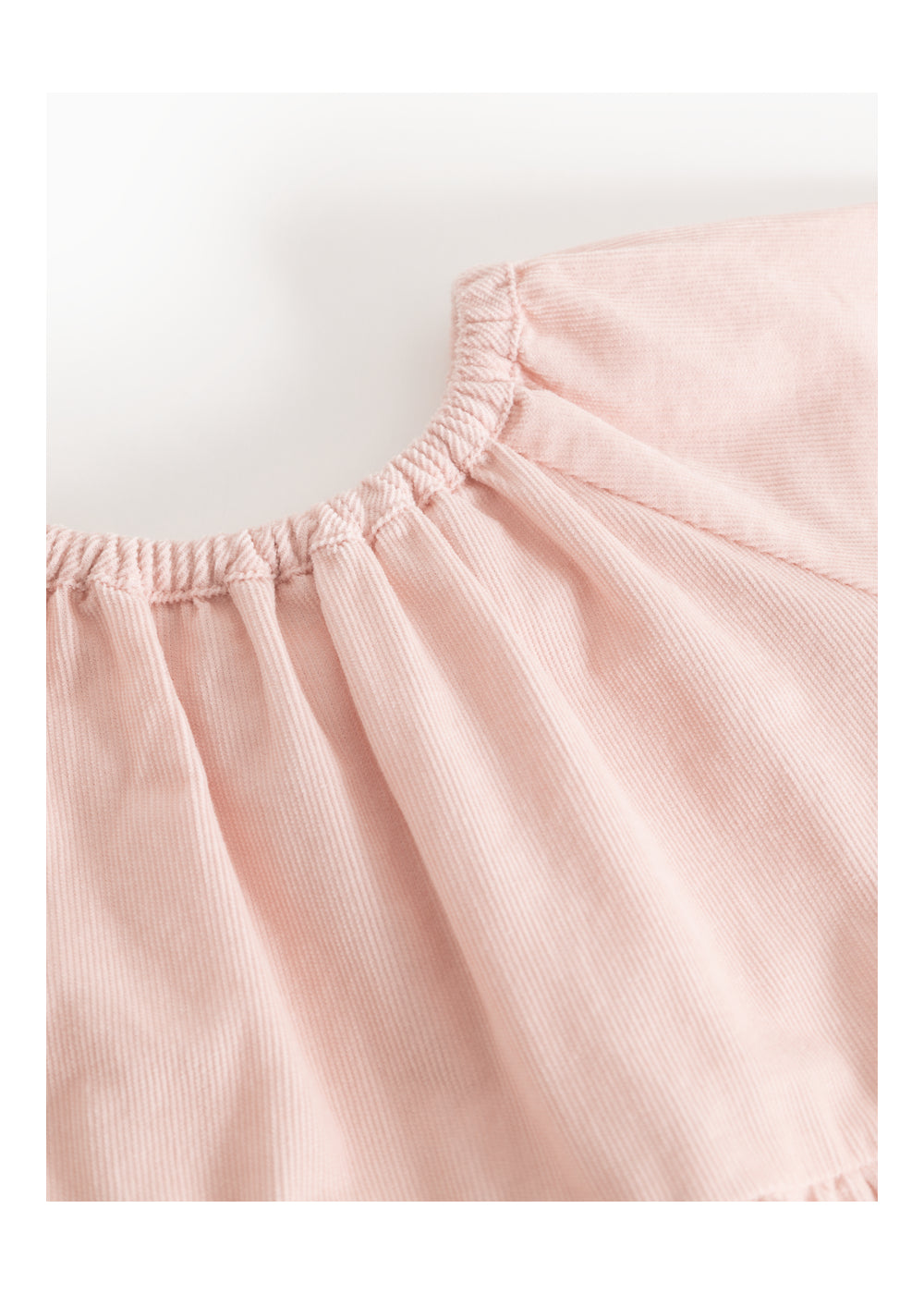 Close-up of a light pink corduroy garment, showing the textured fabric and gathered neckline on a white background.