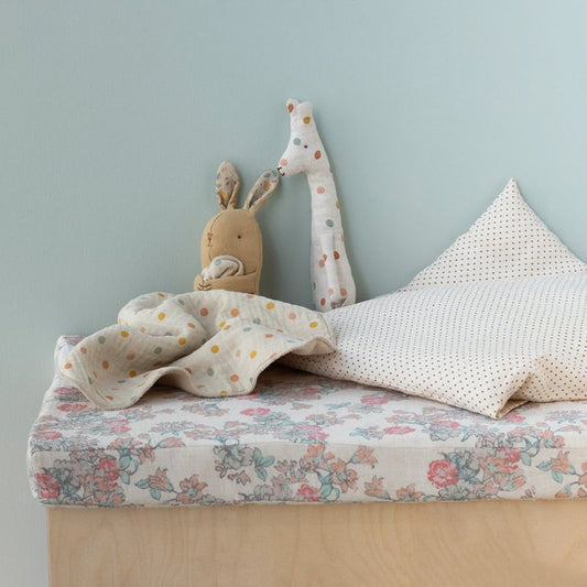 Children's bed with floral bedding, plush toys, and a light blue wall.