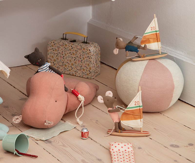 Children's toys including a teddy bear, sailboat, and beach ball on a wooden floor.