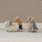 Miniature toy figures of a family with a baby in a stroller against a floral wallpaper background.