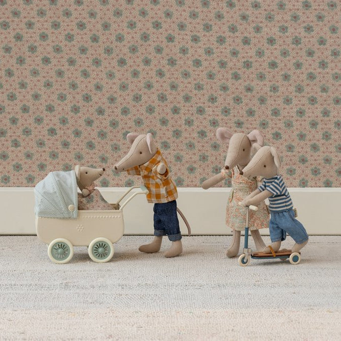 Miniature toy figures of a family with a baby in a stroller against a floral wallpaper background.