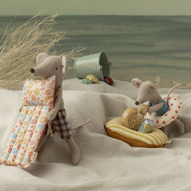 Two toy mice on a sandy beach with a bucket and sand toys in the background.