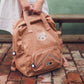 Person holding a brown backpack with a cat design on a brick floor.