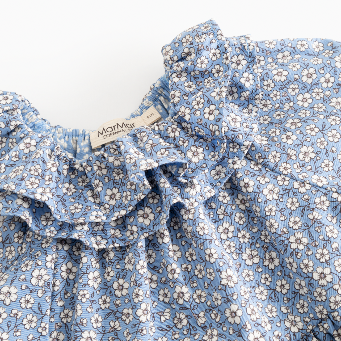 Close-up of a blue floral print garment with ruffled trim and a visible Mommy Jane brand label.