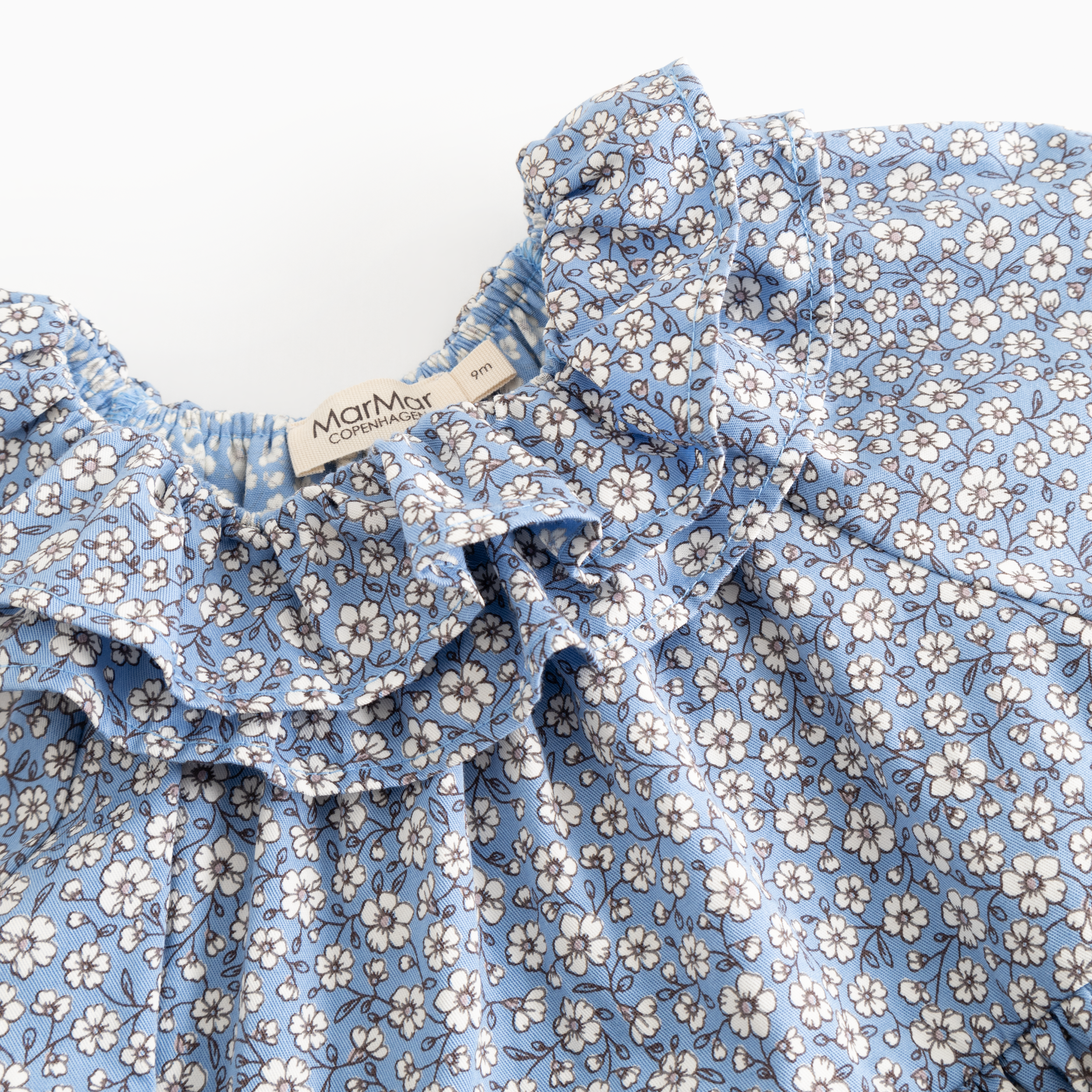 Close-up of a blue floral print garment with ruffled trim and a visible Mommy Jane brand label.