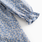 Close-up of a blue fabric garment with a small white and beige floral print and a gathered elastic cuff on the sleeve, shown against a light gray background.