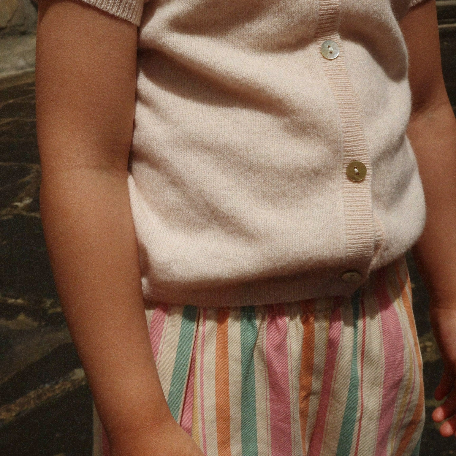 Girls  wearing a light pink cardigan with buttons, and Frankie Pants standing against a dark background.
