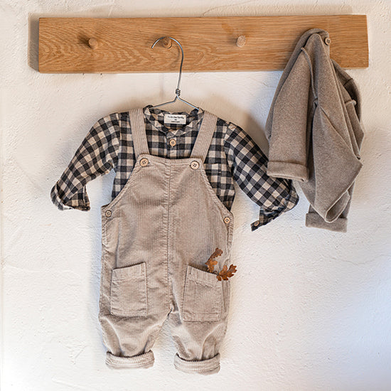 A pair of taupe dungarees for baby boy with a check shirt and taupe cardigan