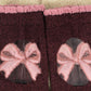 A close-up of a pair of dark burgundy knit socks with pink ribbed cuffs and a pink bow motif on the front, set against a cream-colored knit background.