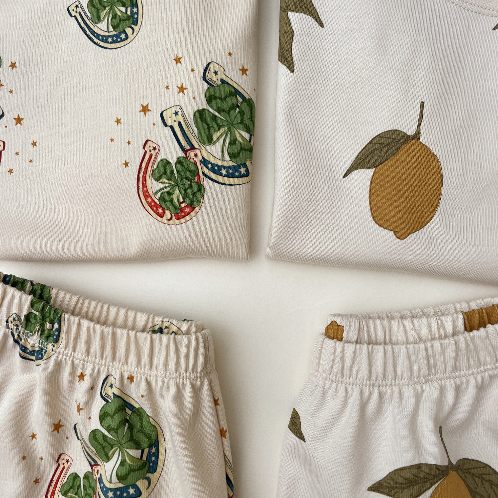 Children's clothing with lucky horseshoe, four-leaf clover, and lemon designs on a white background.