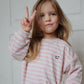 Girll wearing a pink and white striped outfit with a cherry design, making a peace sign.