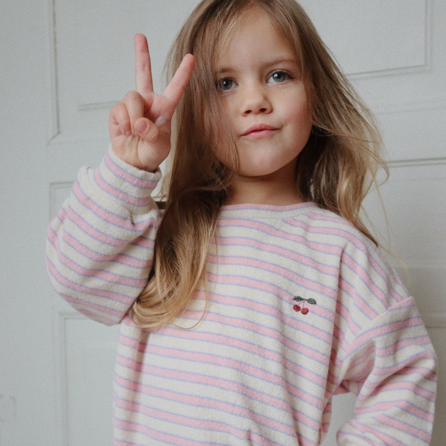 Girll wearing a pink and white striped outfit with a cherry design, making a peace sign.