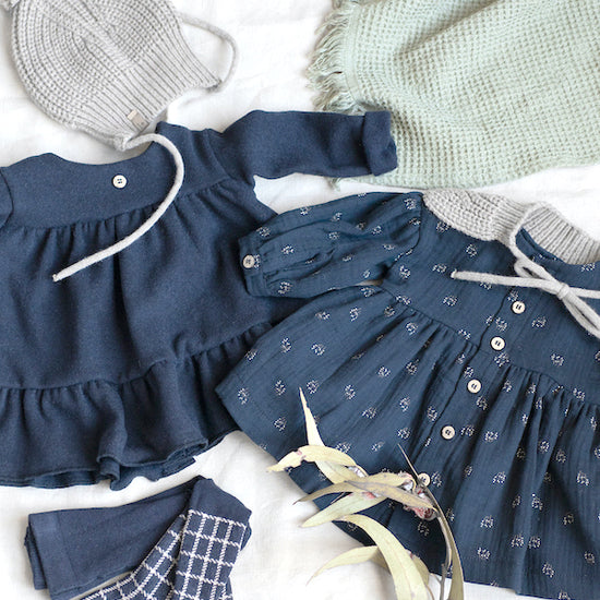 A collection of dark blue dresses for baby girls, along with a hat, stockings and blanket
