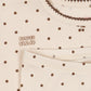 Close-up of a cream-colored baby top with brown polka dots, featuring the brand name 'KONGES SLOJD' embroidered on the chest and a decorative brown ruffled collar.