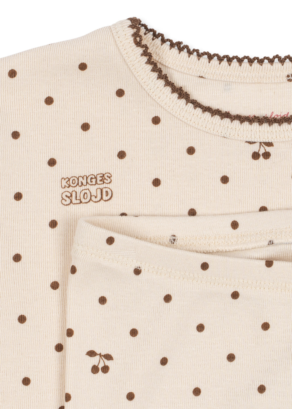 Close-up of a cream-colored baby top with brown polka dots, featuring the brand name 'KONGES SLOJD' embroidered on the chest and a decorative brown ruffled collar.