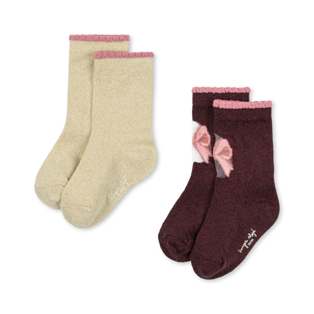 Two pairs of fuzzy crew socks on a white background: one pair is light beige with a pink ribbed cuff, and the other pair is dark burgundy with a pink ribbed cuff and a pink bow detail.
