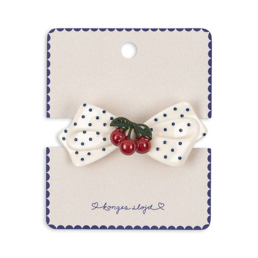 Polka dot bow hair clip with cherries on a branded card against a white background