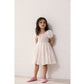 Young girl wearing a white dress with puffed sleeves against a plain background
