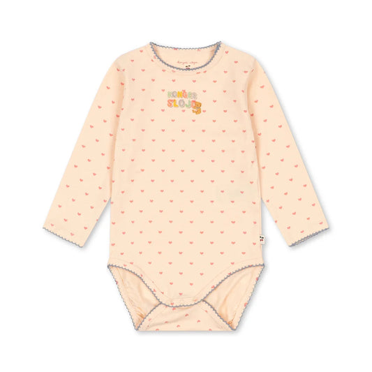 A long-sleeve baby bodysuit in a pale peach-pink color, featuring a small repeating pattern of tiny red hearts and a colorful 'maman loge' graphic on the chest. The garment has gray trim along the collar, cuffs, and leg openings, and is displayed flat against a solid white background.