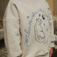 Person wearing a beige hoodie with a fox design and text outdoors.