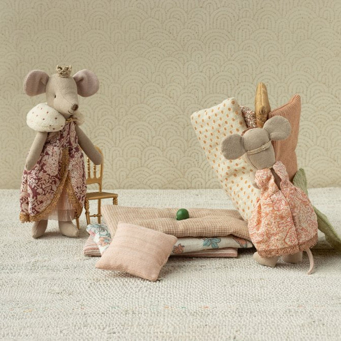 Two plush mouse toys with decorative clothing on a textured surface with a patterned wall background.