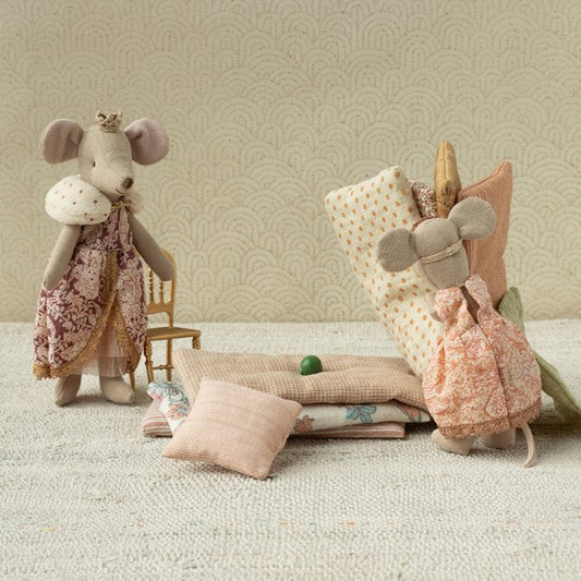 Two plush mouse toys with decorative clothing on a textured surface with a patterned wall background.