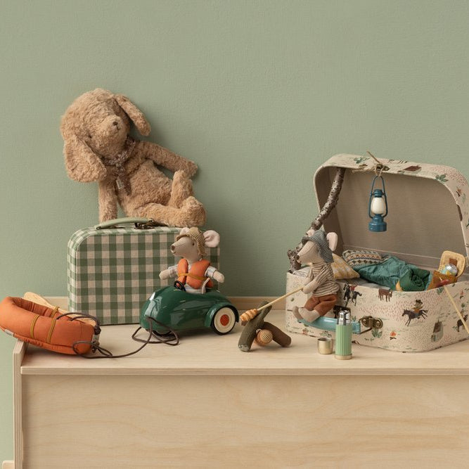 Collection of toys including a teddy bear, toy car, and playset on a wooden surface with a green wall background.