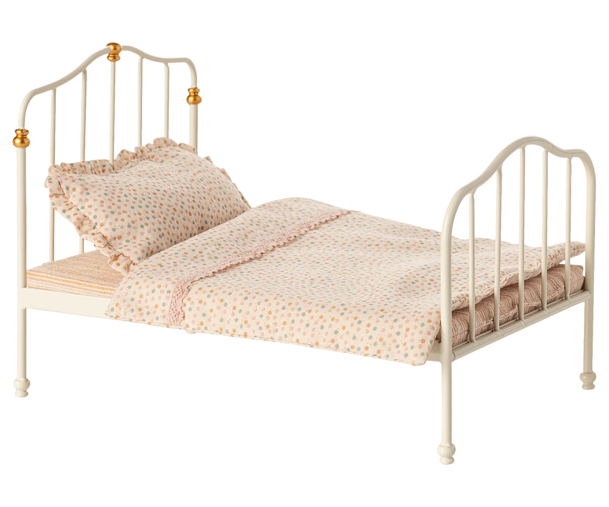 Small bed with white metal frame and pink bedding on a white background