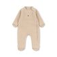 A baby's long-sleeve footed sleeper in a soft, textured beige fleece fabric, featuring a small embroidered animal logo on the left chest, displayed against a solid white background.