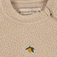 Close-up of a beige sherpa fleece zip-up sweater with a small embroidered yellow lemon and green leaf on the chest. The brand label 'KONGES SLOJ' is visible inside the collar.