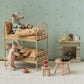 A miniature dollhouse-style room scene with two plush mouse figures arranged on a wooden bunk bed, alongside small furniture pieces, a wallpapered wall, and a fireplace display.