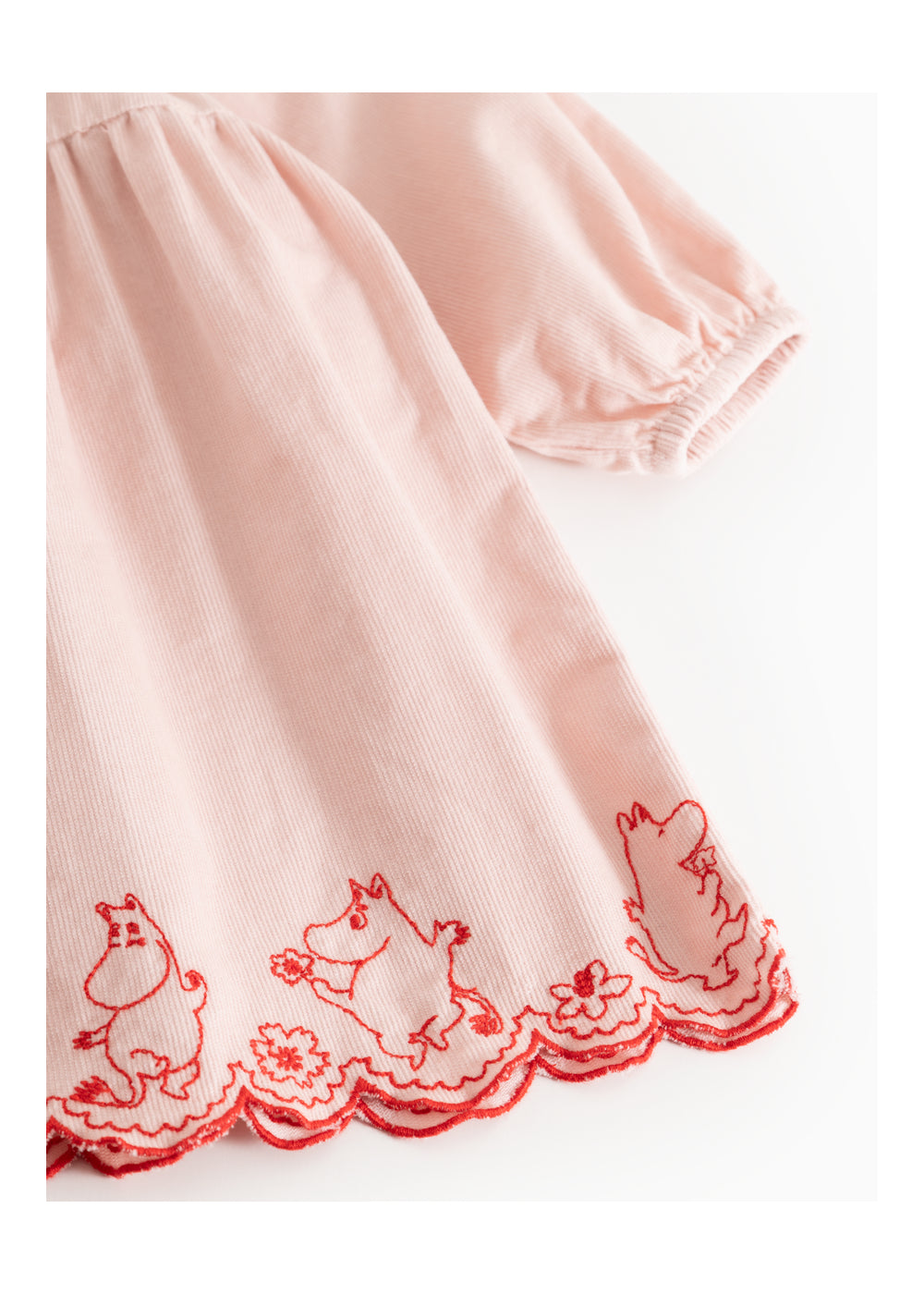A close-up of a light pink fabric garment, likely a dress or nightgown, featuring red embroidered cartoon dog characters and a scalloped red border along the hem.