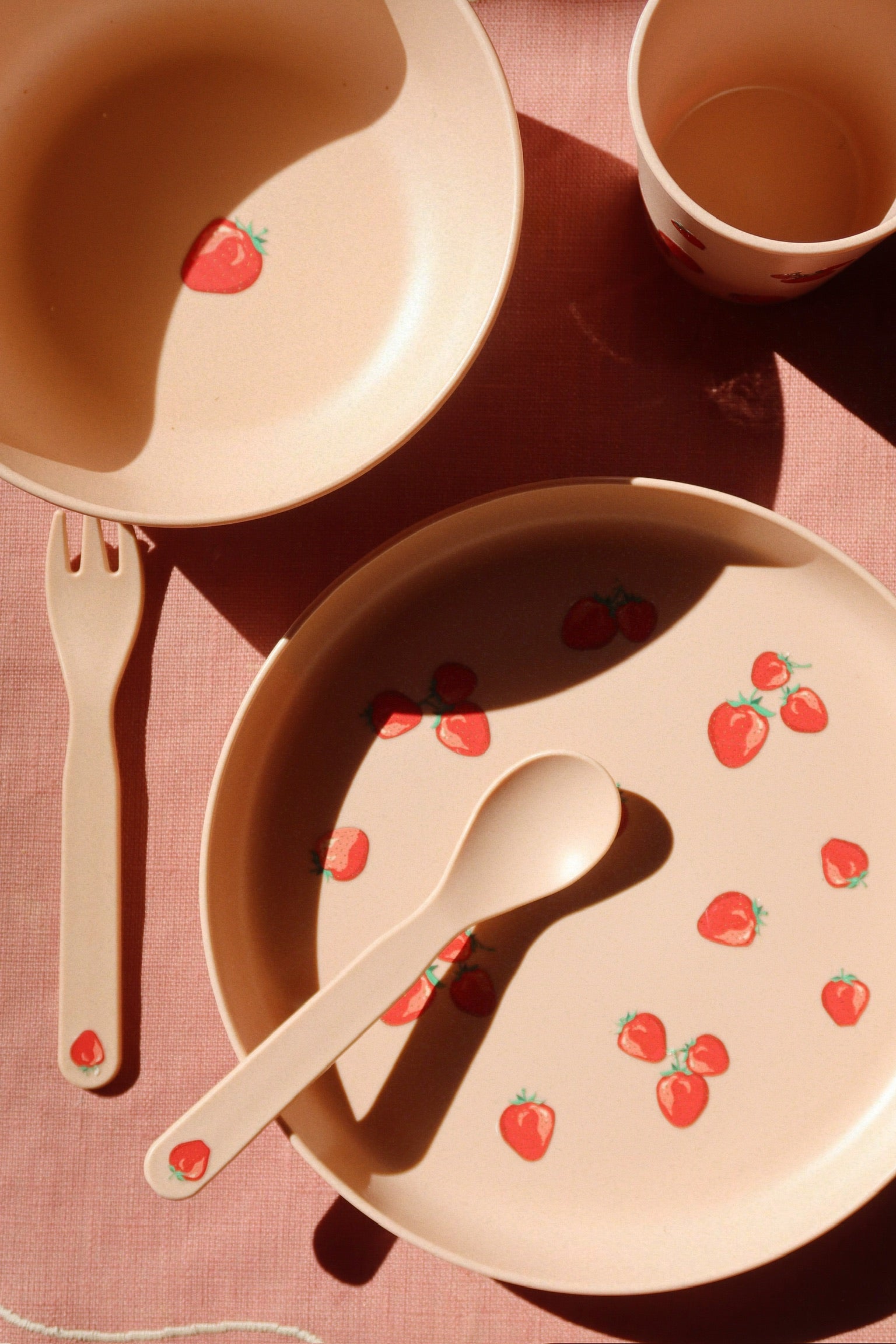 Children's tableware set with strawberry pattern on a pink surface