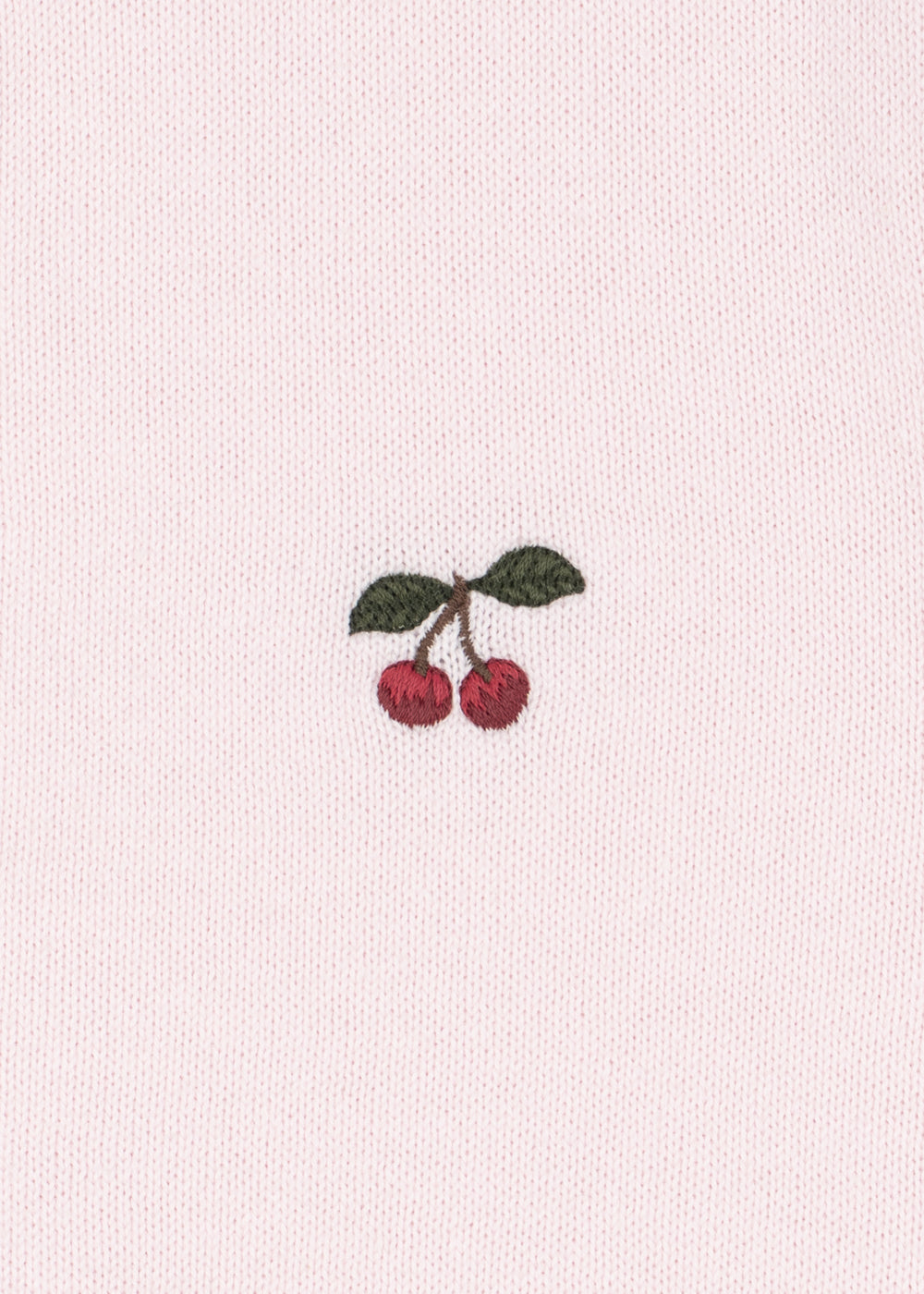 A close-up of a light pink textured fabric featuring a small embroidered motif of two red cherries with green leaves.