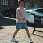 Child standing on a cobblestone street with a building and cars in the background